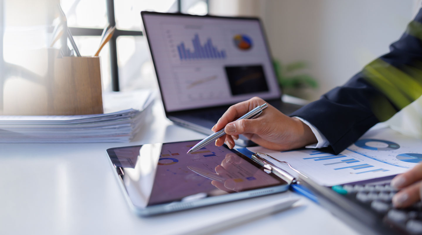 Bureau de travail avec calculatrice, documents financiers français de l'URSSAF, bulletins de paie et ordinateur affichant un tableur de calculs de charges sociales et cotisations